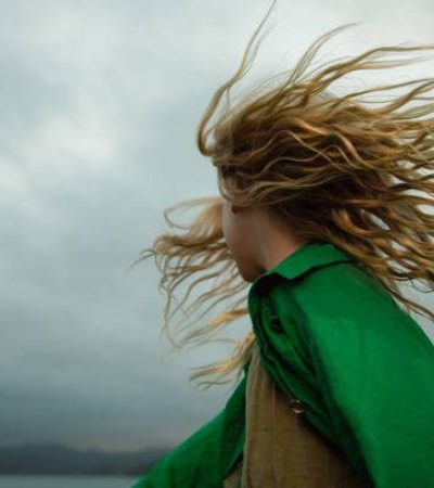 Person with windswept hair wearing green cloak